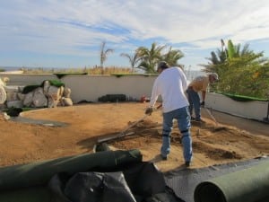 two installers spread dirt on rooftop putting green installation
