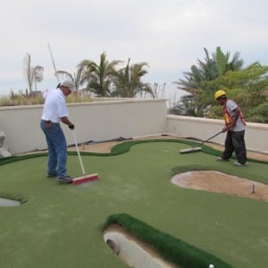 two men sweeping sand infill on rooftop putting green