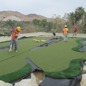 three men installing and sweeping rooftop putting green